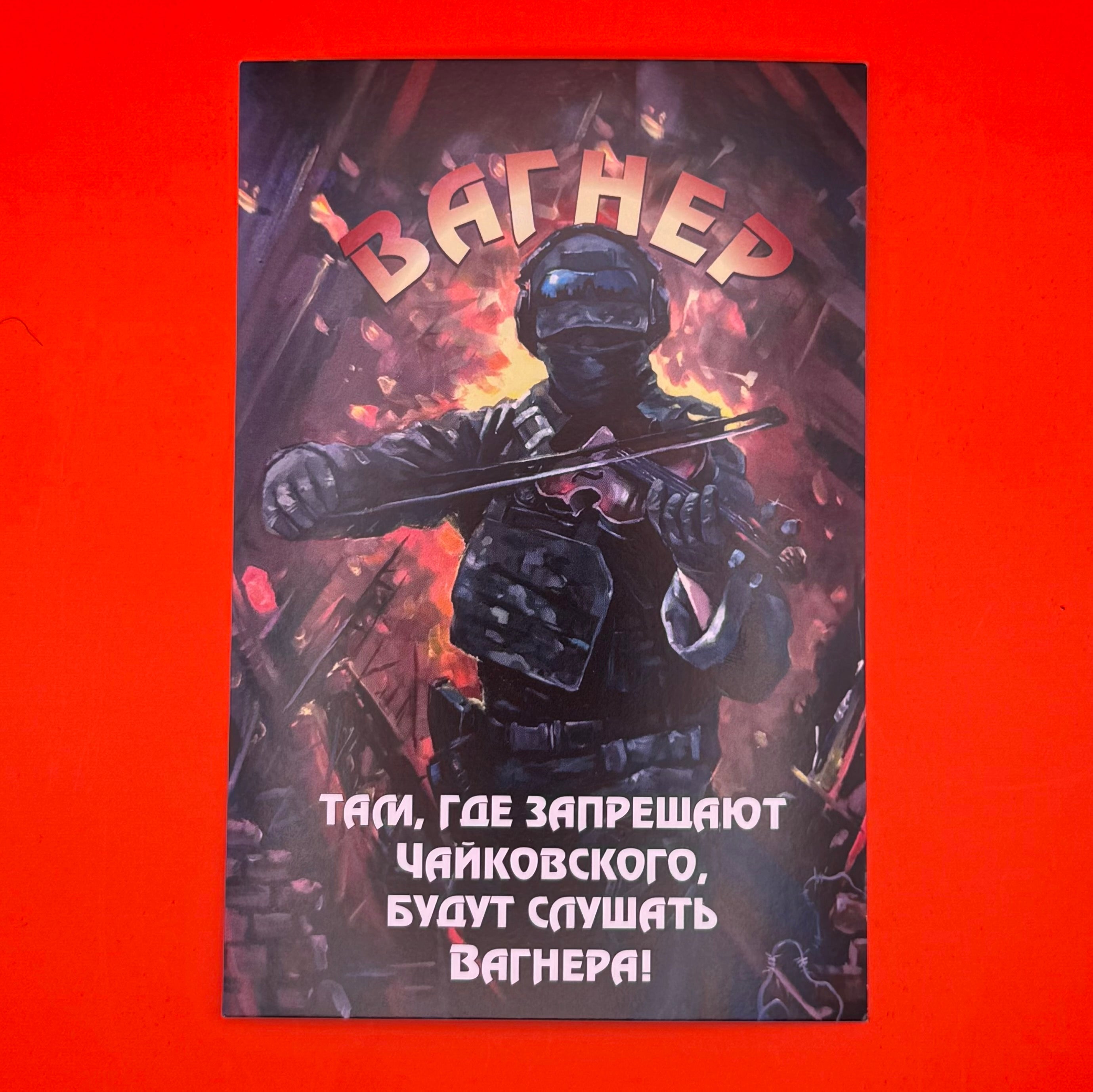 Limited edition Wagner PMC commemorative postcard, depicting a masked fighter playing a violin amidst urban rubble with the phrase 'Where Tchaikovsky is banned, they will listen to Wagner.' This collectible captures Wagner's modern mythos, blending militant symbolism with cultural defiance, ideal for collectors of political ephemera and modern conflict memorabilia.