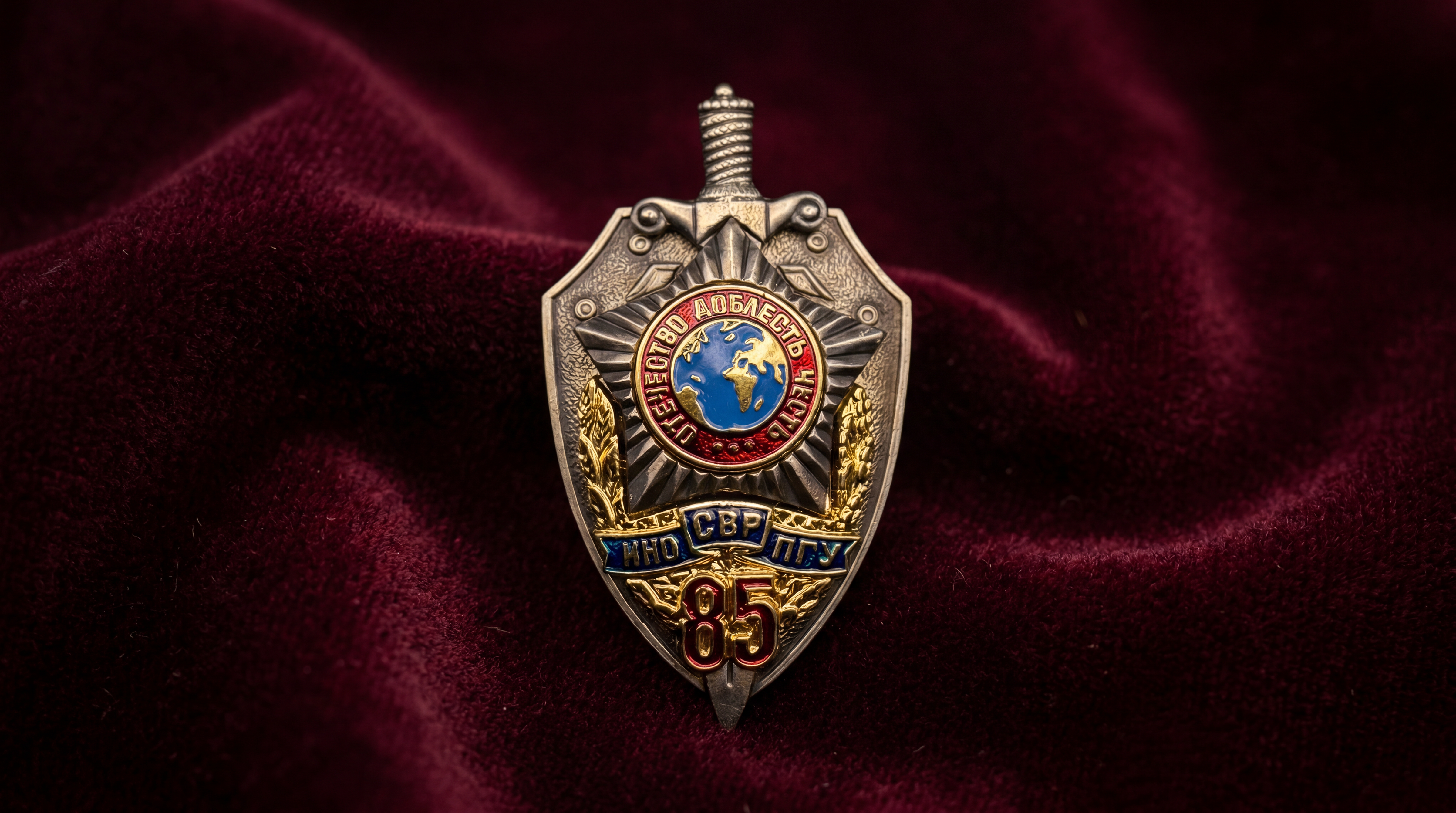 Russian SVR foreign intelligence 85th anniversary badge marked INO SVR PGU with sword, shield, and enamel globe on burgundy background